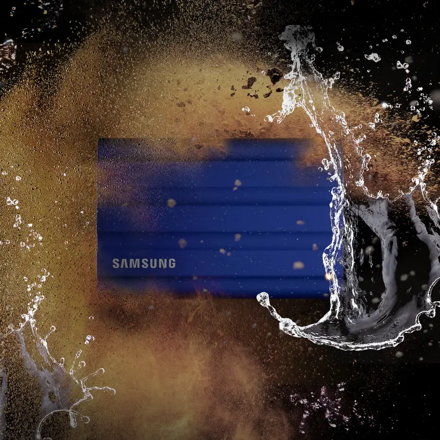 Samsung T7 Shield SSD in Blau, umgeben von Wasser- und Staubpartikeln auf dunklem Hintergrund – Key Visual zur Bewerbung der Robustheit